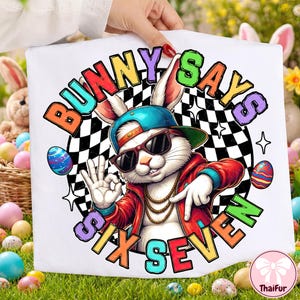 Pode incluir: Camiseta gráfica branca com um coelho legal usando óculos de sol, boné azul e jaqueta vermelha. O texto "Bunny Says Six Seven" está em letras coloridas, com ovos de Páscoa e um fundo quadriculado.