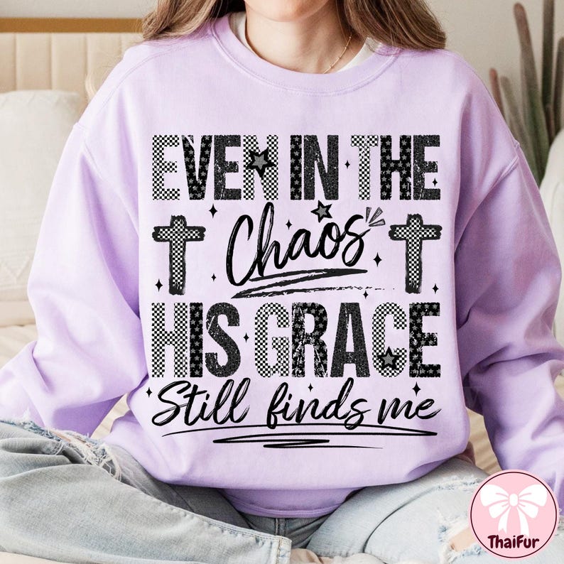May include: A light purple sweatshirt with the text "EVEN IN THE Chaos HIS GRACE Still finds me" in black and white. The text includes cross symbols and star accents. The sweatshirt has long sleeves.