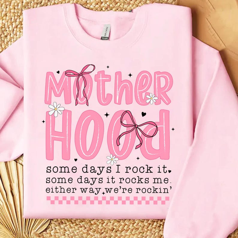 May include: Pink sweatshirt with the text "Mother Hood" in pink letters with a pink bow and flowers. The text below reads "some days I rock it, some days it rocks me, either way, we're rockin'."