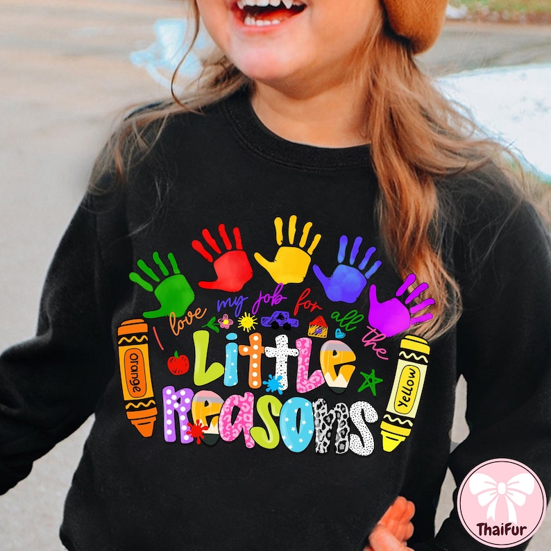 May include: Black sweatshirt with a colorful graphic design. The design includes handprints in green, red, yellow, blue, and purple, along with the text "I love my job for all the Little Reasons" and crayon illustrations.