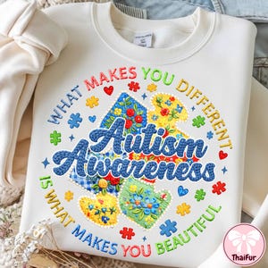 May include: White sweatshirt with colorful embroidered text and designs. The design includes the words "Autism Awareness" surrounded by the phrase "What makes you different is what makes you beautiful." Features puzzle pieces, hearts, and floral patterns.