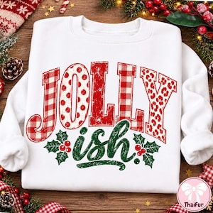 May include: A white long-sleeve sweatshirt featuring the red text JOLLY in a distressed font with varied patterns including buffalo plaid, polka dots, and leopard print. Below, the word ish is printed in green with holly leaf accents.