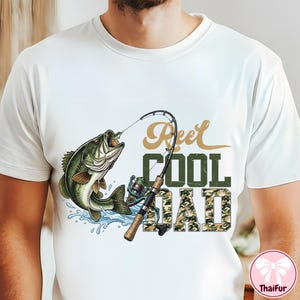 May include: White t-shirt featuring a graphic of a largemouth bass jumping out of water, with a fishing rod and the text "Reel Cool Dad". The text "COOL" is in green, and "DAD" is in a camouflage pattern.