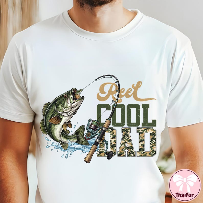 May include: White t-shirt featuring a graphic of a largemouth bass jumping out of water, with a fishing rod and the text "Reel Cool Dad". The text "COOL" is in green, and "DAD" is in a camouflage pattern.