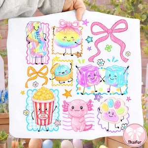 Puede incluir: Una tela blanca con un estampado gráfico colorido de varios personajes de dibujos animados, incluyendo una barra de mantequilla, una empanadilla, palomitas, un ajolote y una huella, con lazos rosas, estrellas y flores en un estilo vibrante.