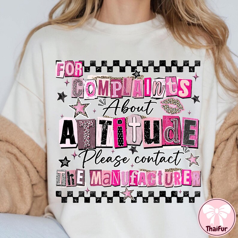 May include: Cream-colored t-shirt with a graphic design that reads "FOR COMPLAINTS ABOUT ATTITUDE Please contact THE MANUFACTURER." The text is in various fonts and colors, including pink, black, and leopard print, with star accents.