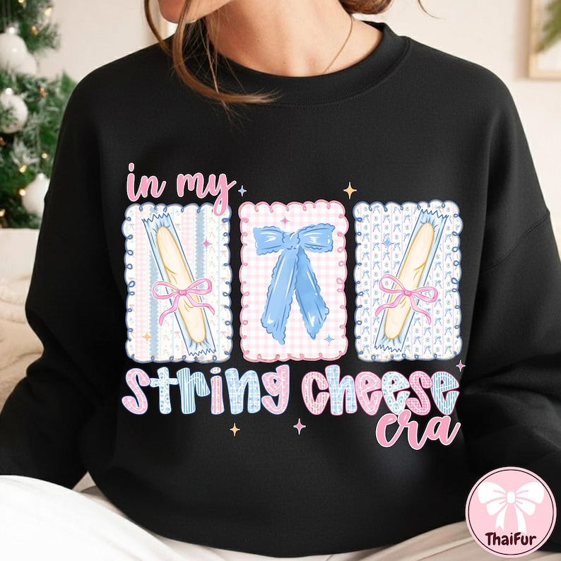 Może przedstawiać: Czarna bluza z nadrukiem graficznym z napisem "in my string cheese era". Projekt zawiera trzy oprawione obrazy z serem w sznurkach i niebieską kokardą. Tekst i obrazy są w kolorze r&oacute;żowym i niebieskim.