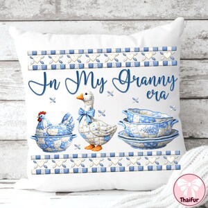 May include: White decorative pillow with a blue and white floral design. The pillow features a hen, a goose with a blue bow, and a stack of dishes. The text "In My Granny era" is written in blue script across the pillow.