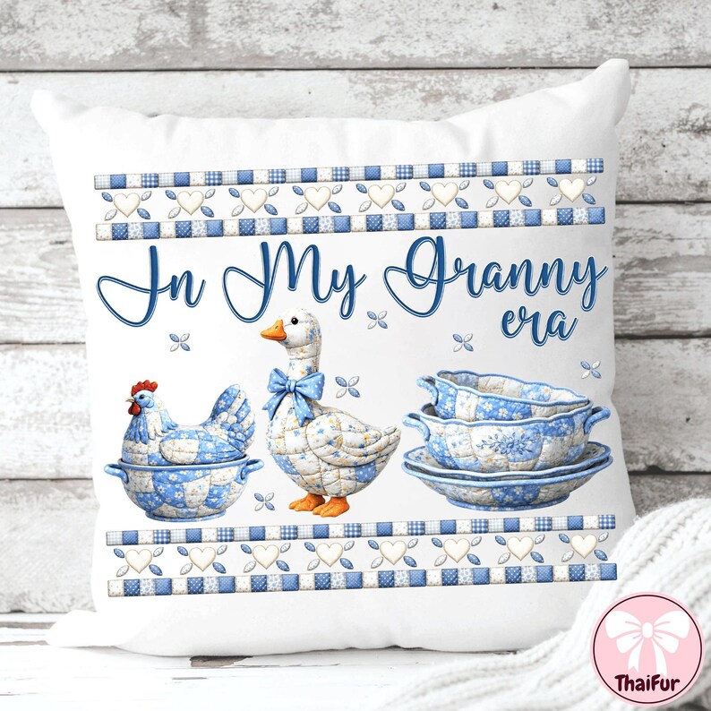 May include: White decorative pillow with a blue and white floral design. The pillow features a hen, a goose with a blue bow, and a stack of dishes. The text "In My Granny era" is written in blue script across the pillow.