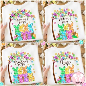 以下が含まれることがあります： 「Grammy's peeps」「Mimi's peeps」「Grandma's peeps」「Nana's peeps」の文字とカラフルな木のイラストがプリントされた白いスウェットシャツ。バスケットに入った漫画のウサギのデザインで、下に名前が書かれています。イースターをテーマにしたアパレル。
