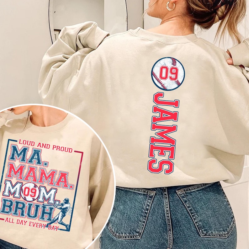 May include: A beige sweatshirt with a baseball graphic and the name "JAMES" printed vertically down the back. The front of the sweatshirt has a graphic with the text "LOUD AND PROUD MA. MAMA. MOM BRUH ALL DAY EVERY DAY" and a baseball player illustration.