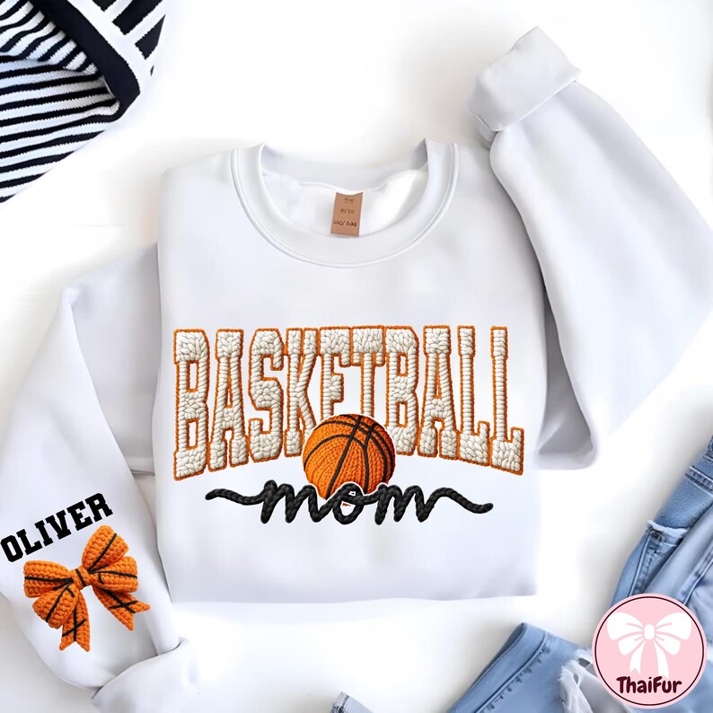 Puede incluir: Sudadera blanca con el texto bordado "BASKETBALL mom" y un gr&aacute;fico de baloncesto. La palabra "OLIVER" est&aacute; bordada en la manga izquierda, junto con un lazo en forma de baloncesto. La sudadera tiene mangas largas.
