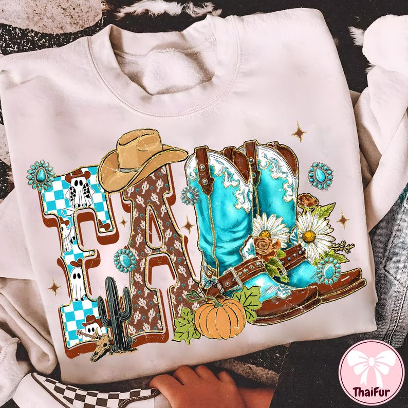 May include: Cream-colored sweatshirt with a graphic design featuring the word "FA" in a Western style. The design includes a cowboy hat, turquoise cowboy boots, a pumpkin, and a cactus. The letters are decorated with a checkered pattern and a brown pattern.