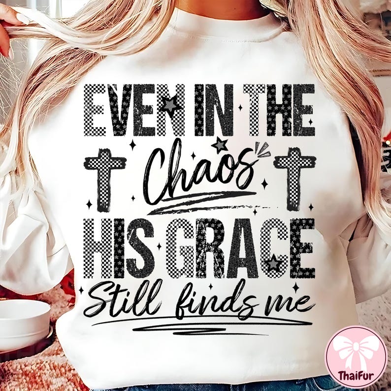 May include: White sweatshirt with the text "EVEN IN THE Chaos HIS GRACE Still finds me" in black. The text includes cross and star graphics. The sweatshirt has a crew neck.