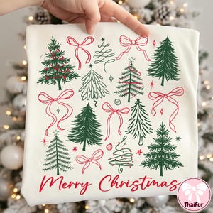 Puede incluir: Un textil crema con temática navideña con un patrón de árboles de Navidad verdes y lazos rojos. Las palabras "Merry Christmas" están escritas en rojo en la parte inferior. El diseño está sostenido por una mano.