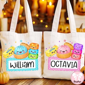 Può includere: Due borse in tela bianca con grafiche animate colorate di dim sum in cestini di bambù, panetti di burro etichettati 4oz e macaron impilati. Una borsa riporta il nome William, l'altra Octavia, entrambi scritti in caratteri neri.