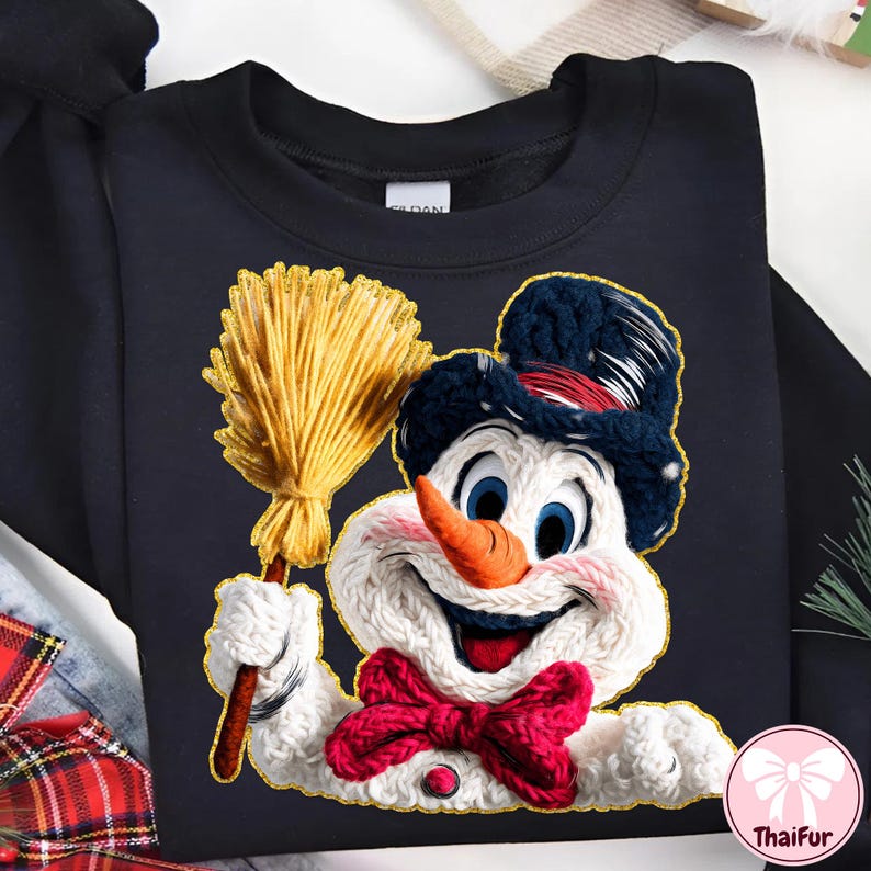 May include: Black sweatshirt with a smiling snowman design. The snowman has a carrot nose, blue eyes, and a red bow tie. He is holding a yellow broom. The design is outlined in gold.