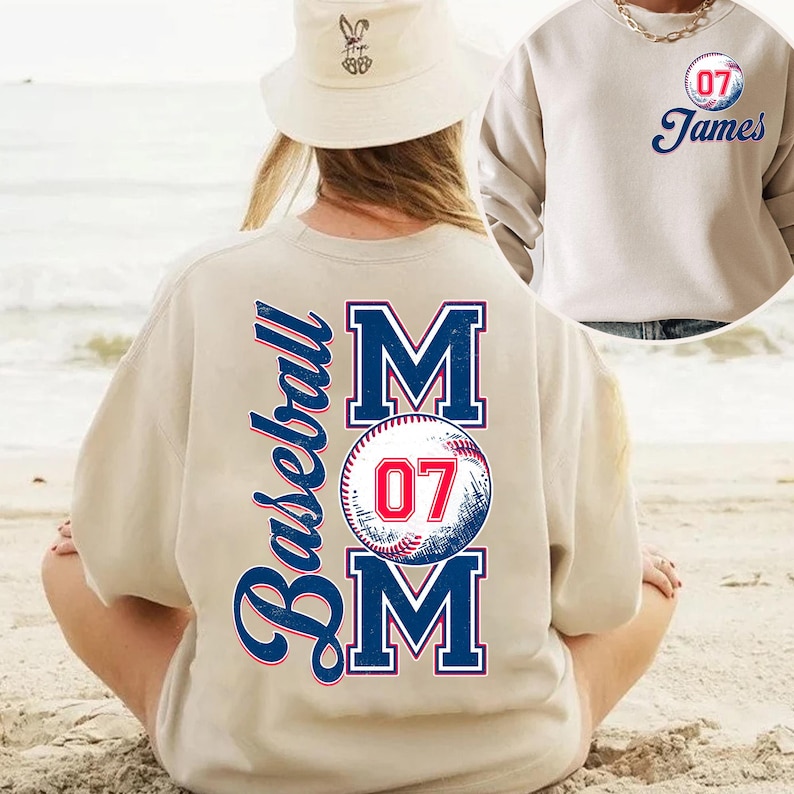 May include: A beige sweatshirt with the words "Baseball Mom" and a baseball with the number "07" printed on the back. The front of the sweatshirt has a small circle with the number "07" and the name "James" printed on it.