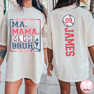 May include: White t-shirt with a baseball theme. The front of the shirt has the text "Loud and Proud" and "Ma. Mama. Mom.  Bruh." with a baseball and a baseball player graphic. The back of the shirt has the number "09" and the name "James" in red with a baseball graphic.