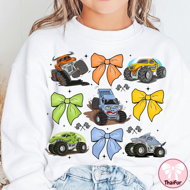 K&ouml;nnte beinhalten: Wei&szlig;es Sweatshirt mit bunten Monstertruck-Grafiken und dekorativen Schleifen. Die Monstertrucks sind in Orange, Gelb, Gr&uuml;n und Blau gehalten und haben gro&szlig;e Reifen und aggressive Designs. Die Schleifen sind orange, gr&uuml;n, gelb und blau.