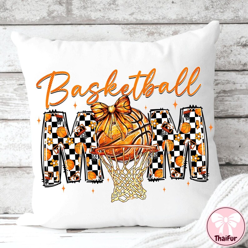 May include: White decorative pillow with the words "Basketball Mom" in orange script. The design features a basketball with a bow, a net, and the letters "MOM" with basketball and floral patterns.
