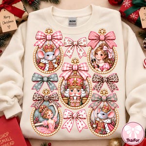 Op de afbeelding: Een crèmekleurig sweatshirt met ronde hals en een grafische print van vijf ovale ornamenten en vijf decoratieve strikken. De ornamenten bevatten illustraties van een muizenkoning, een meisje, een notenkraker, een ballerina en een muizensoldaat.