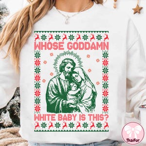 May include: White sweatshirt with a green and red Christmas sweater design. The graphic features a religious image and the text "WHOSE GODDAMN WHITE BABY IS THIS?" in red. The design includes reindeer and snowflake patterns.