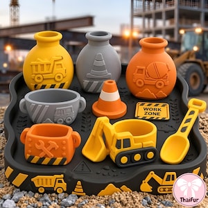 Op de afbeelding: Een bouwset met drie ronde bakjes in geel, grijs en oranje met reliëf van een kiepwagen, verkeerskegel en betonmixer. Inclusief een grijze kom, oranje kegel, gele graafmachine, schep en een Work Zone bordje op een zwart dienblad met motieven.