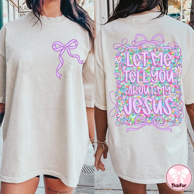 Puede incluir: Una camiseta blanca con un lazo rosa en la parte delantera y el texto "Let me tell you about my Jesus" rodeado de flores en la parte posterior.