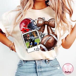 Könnte beinhalten: Cremefarbenes T-Shirt mit Football-Motiv. Das Design umfasst einen roten Helm, einen Football, eine Schleife mit dem Namen "JACSON" und ein Foto eines Footballspielers. Die Nummer "10" ist ebenfalls abgebildet.