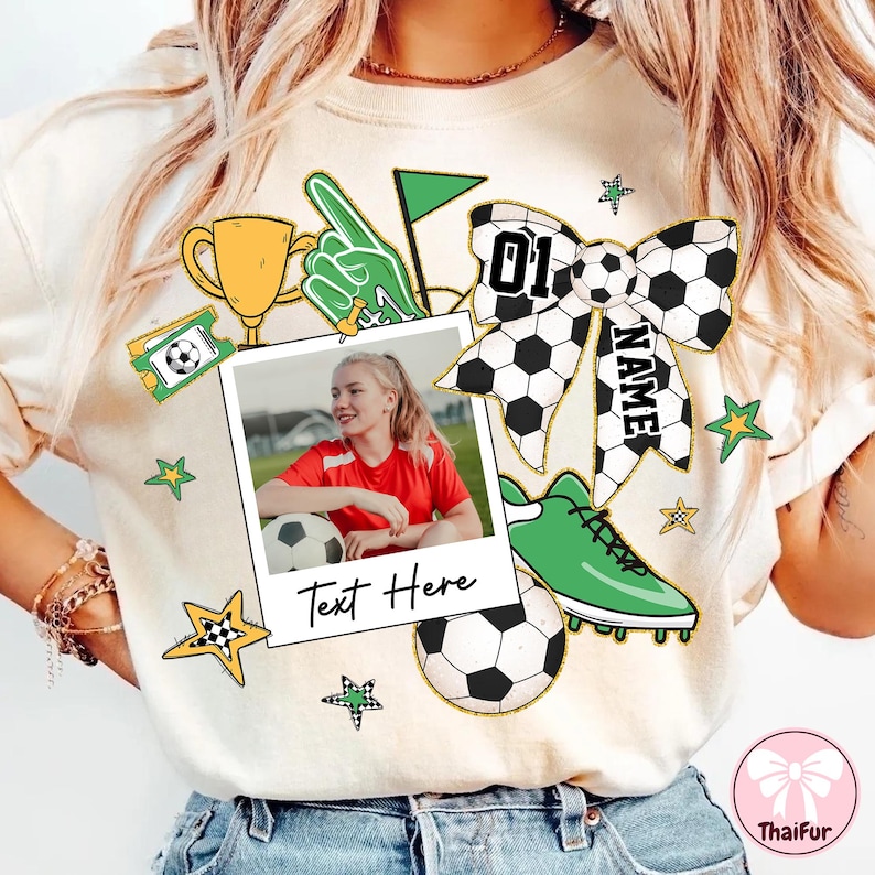 May include: White t-shirt with a green, black, and white soccer-themed design. The design includes a soccer ball, a trophy, a bow with the number "01" and the word "NAME", a green shoe, and a photo frame with the text "Text Here".