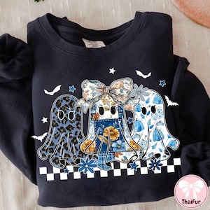 May include: Navy blue sweatshirt featuring three ghost designs with floral, leopard, and patchwork patterns. The ghosts have bows and are decorated with stars, bats, and flowers. A black and white checkered border is at the bottom.