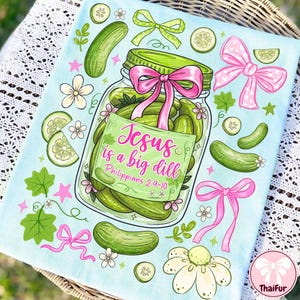 May include: Light blue decorative towel with a jar of pickles illustration. The jar has a green lid and a pink bow. Text on the jar reads "Jesus is a big dill" and "Philippians 2:9-10". The design includes pickles, bows, and flowers.