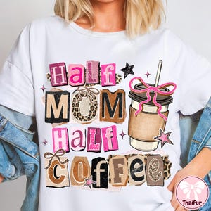 May include: White t-shirt with the text "Half Mom Half Coffee" in pink, brown, and black letters. The design includes a coffee cup with a pink bow and star accents. The shirt has a casual, everyday style.