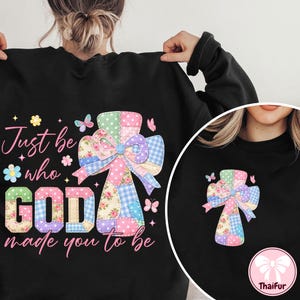 May include: Black sweatshirt featuring a colorful cross design with a patchwork pattern and a bow. The text "Just be who GOD made you to be" is printed in pink and green. Butterflies and floral accents complete the design.