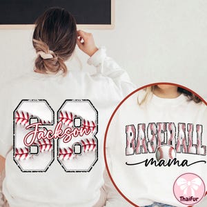 May include: White sweatshirt with a baseball design. The back displays the number "68" with a baseball pattern and the name "Jackson". The front features "Baseball Mama" with a baseball graphic.