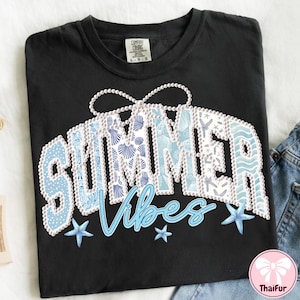 Puede incluir: Camiseta negra Comfort Colors con un diseño "SUMMER Vibes". La palabra "SUMMER" está en azul claro con patrones de conchas marinas, y "Vibes" está en una fuente cursiva. El diseño incluye estrellas de mar y un borde perlado.
