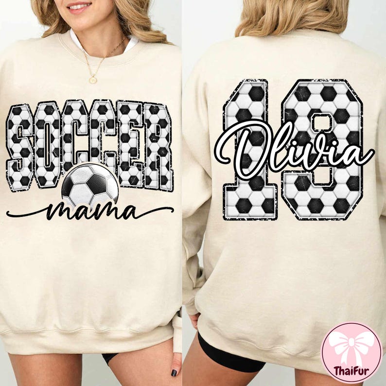 K&ouml;nnte beinhalten: Cremefarbenes Sweatshirt mit dem Schriftzug "SOCCER mama" in schwarzer Schrift und einer Fu&szlig;ballgrafik. Das Wort "SOCCER" ist mit einem Fu&szlig;ballmuster gef&uuml;llt. Auf der R&uuml;ckseite befindet sich die Zahl "19" mit dem Namen "Olivia" in Schrift, ebenfalls mit einem Fu&szlig;ballmuster.