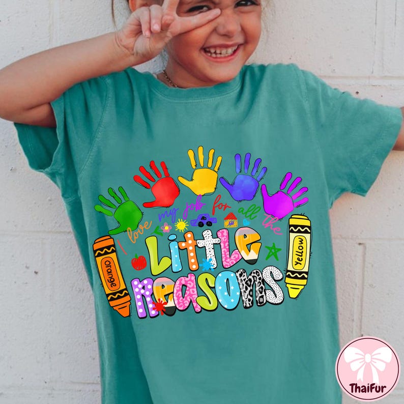May include: Teal t-shirt with a colorful graphic featuring handprints, crayons, and the text "Little Reasons." The design includes the phrase "I love my job for all the." The shirt has a relaxed fit and short sleeves.