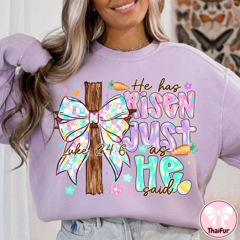 May include: A light purple sweatshirt with a colorful graphic featuring a wooden cross, a bow, carrots, flowers, and the text "He has Risen JUST as HE said" and "Luke 24:6".