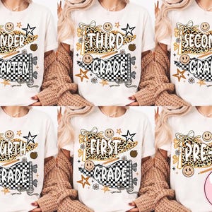 May include: A white t-shirt featuring a graphic design of two pennants, one with a leopard print and one with a black and white checkered pattern. The design includes stars, smiley faces, an apple, and a pencil, with text indicating school grades.