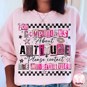 May include: Pink sweatshirt with the text "FOR COMPLAINTS ABOUT ATTITUDE Please contact THE MANUFACTURER" in a mix of fonts and patterns, including leopard print and stars. The design is framed with a black and white checkered pattern.
