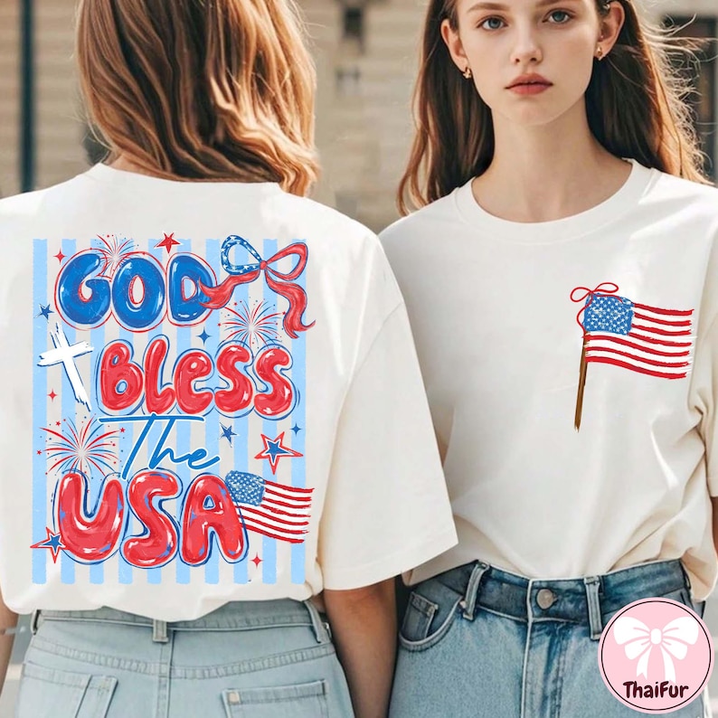 Op de afbeelding: Twee witte t-shirts met patriottische ontwerpen. E&eacute;n shirt heeft de tekst "God Bless The USA" in rood, wit en blauw, met vuurwerk en sterren. Het andere shirt heeft een kleine Amerikaanse vlag op de zak.