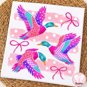 May include: A white square fabric panel featuring three flying ducks in vibrant shades of pink, blue, and purple. The ducks have patterned wings with stars, polka dots, and gingham checks. Pink brushstroke stripes and bows decorate the background.