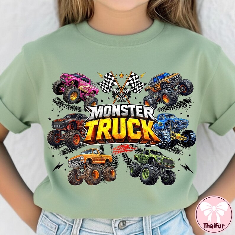 K&ouml;nnte beinhalten: Salbeigr&uuml;nes T-Shirt mit einem farbenfrohen Grafikdesign von sechs Monster Trucks in verschiedenen Farben und dem Text "MONSTER TRUCK". Das Design umfasst karierte Flaggen und Sterne.