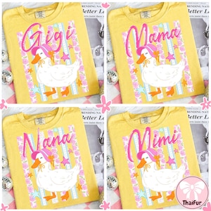 Puede incluir: Camisetas amarillas con un gráfico de pato con un sombrero rosa. Las camisetas tienen los nombres "Gigi", "Mama", "Nana" y "Mimi" en escritura rosa. El pato es blanco con patas y pico naranjas. Acentos florales y de estrellas.