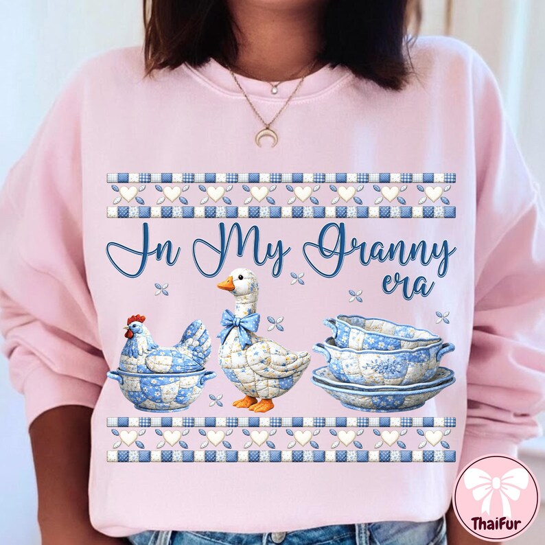 May include: Pink sweatshirt with the text "In My Granny era". The design features a chicken, a goose with a blue bow, and a serving dish, all with blue and white floral patterns. Decorative blue and white borders.