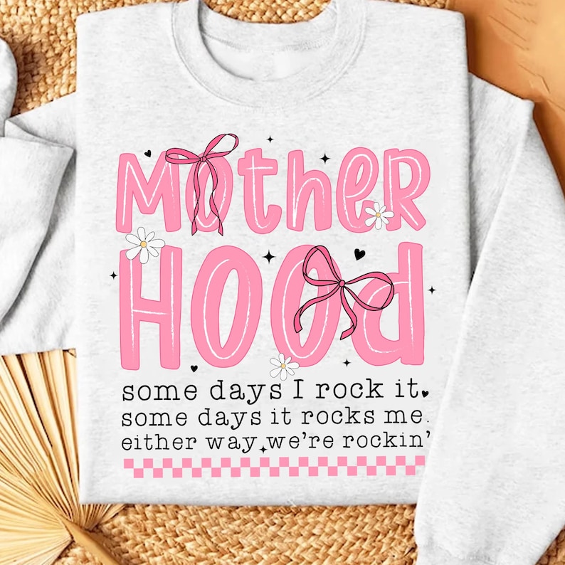 May include: A white sweatshirt with a pink graphic that says "Mother Hood" with pink bows and flowers. The text below says "some days I rock it, some days it rocks me, either way we're rockin'."
