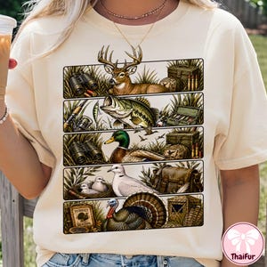 May include: A cream-colored t-shirt featuring a graphic print divided into five horizontal panels. The panels depict a deer, a bass, a mallard duck, a dove, and a turkey, each accompanied by outdoor gear like binoculars, tackle boxes, and ammunition.