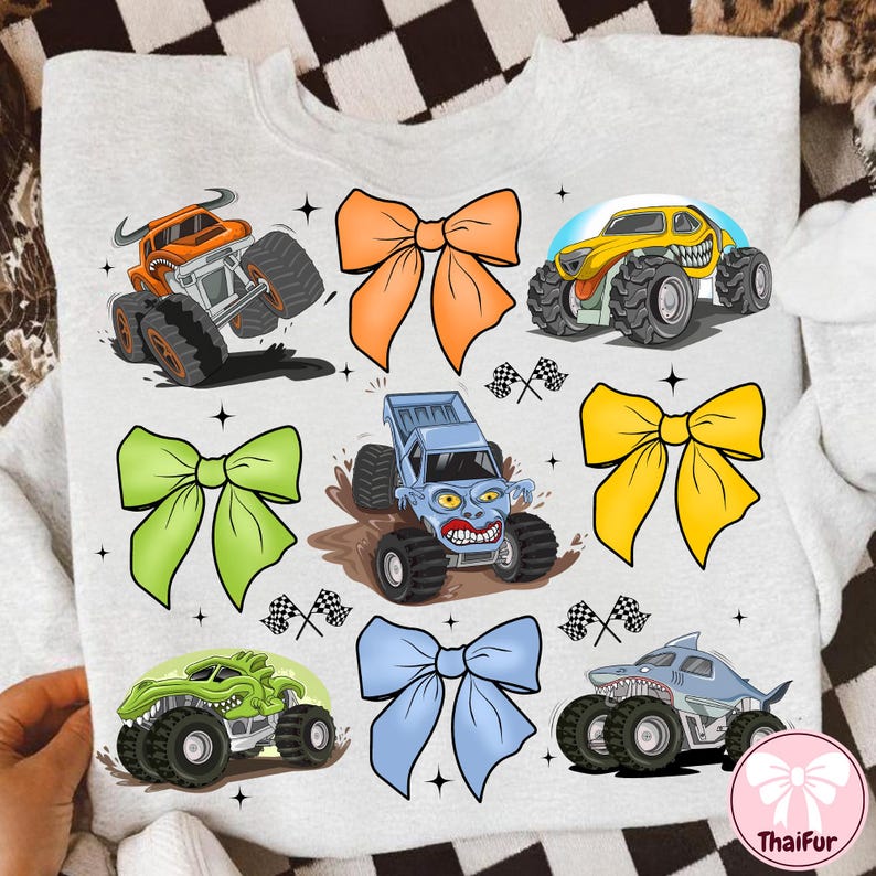 K&ouml;nnte beinhalten: Ein hellgraues Sweatshirt mit bunten Cartoon-Monstertrucks und Schleifen. Die Monstertrucks sind in Orange, Gelb, Gr&uuml;n, Blau und Grau gehalten und haben gro&szlig;e Reifen und aggressive Gesichtsausdr&uuml;cke. Die Schleifen sind orange, gr&uuml;n, gelb und blau.
